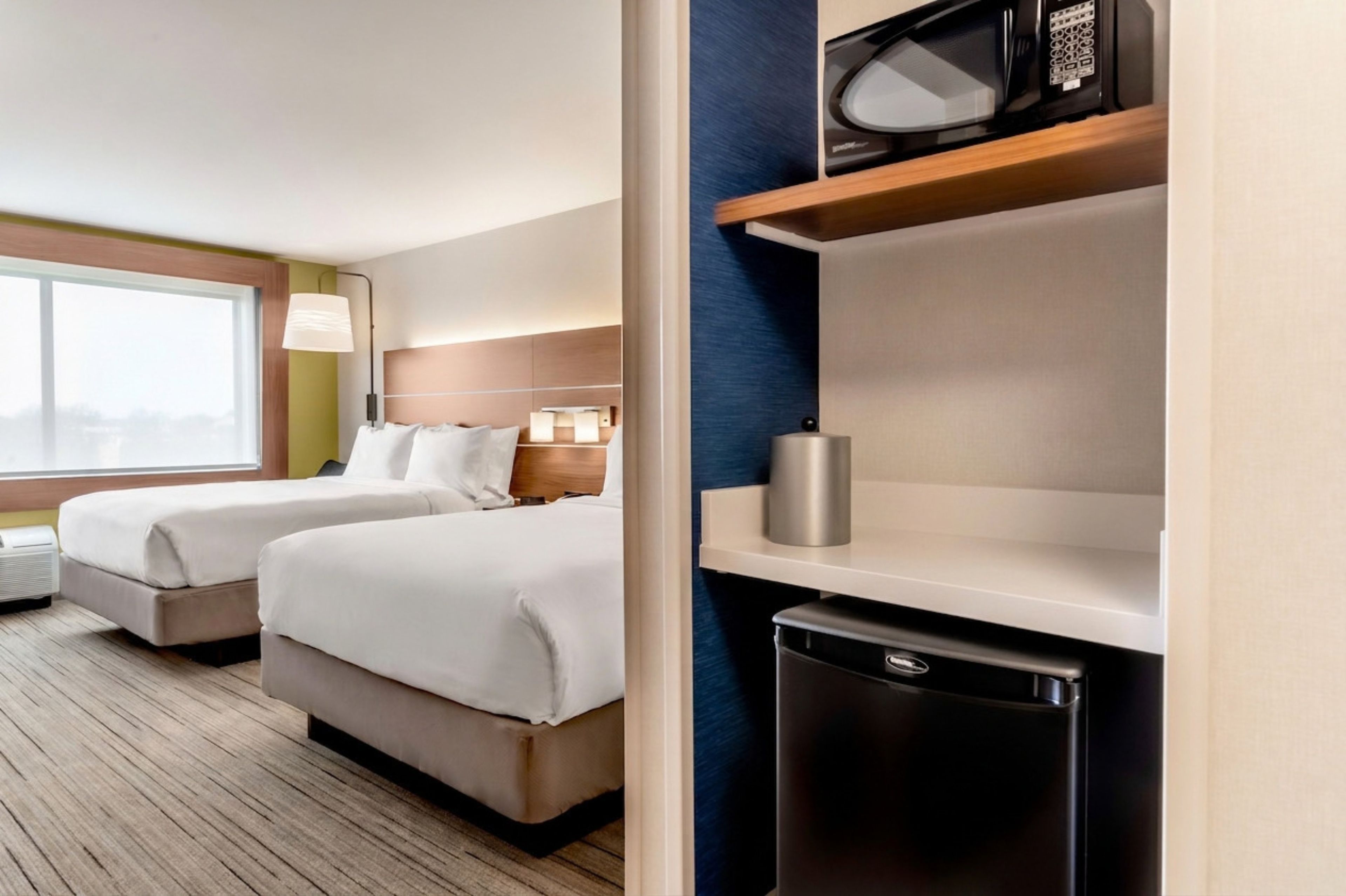 Habitación de hotel con dos camas, microondas, un refrigerador pequeño y ventana con vistas.