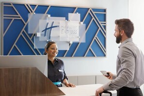 A hotel reception desk with a modern design, a digital display board, and a name tag on the staff member.