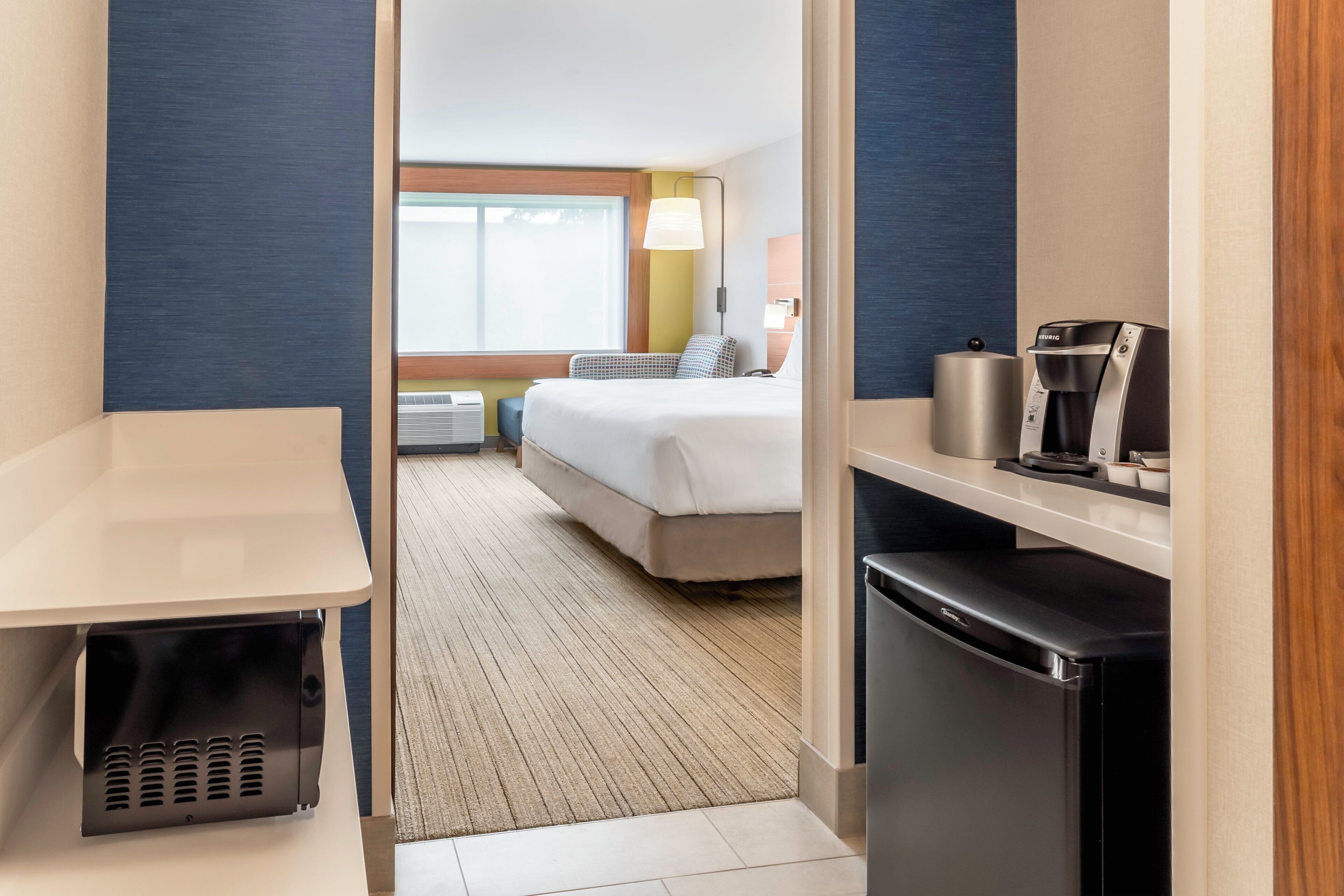 Een hotelkamer met een bed, nachtkastje, koffiezetapparaat en een prullenbak.