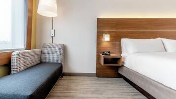 Habitació d'hotel amb un llit, una taula de treball amb un telèfon, una cadira, una làmpada i una finestra amb cortines.