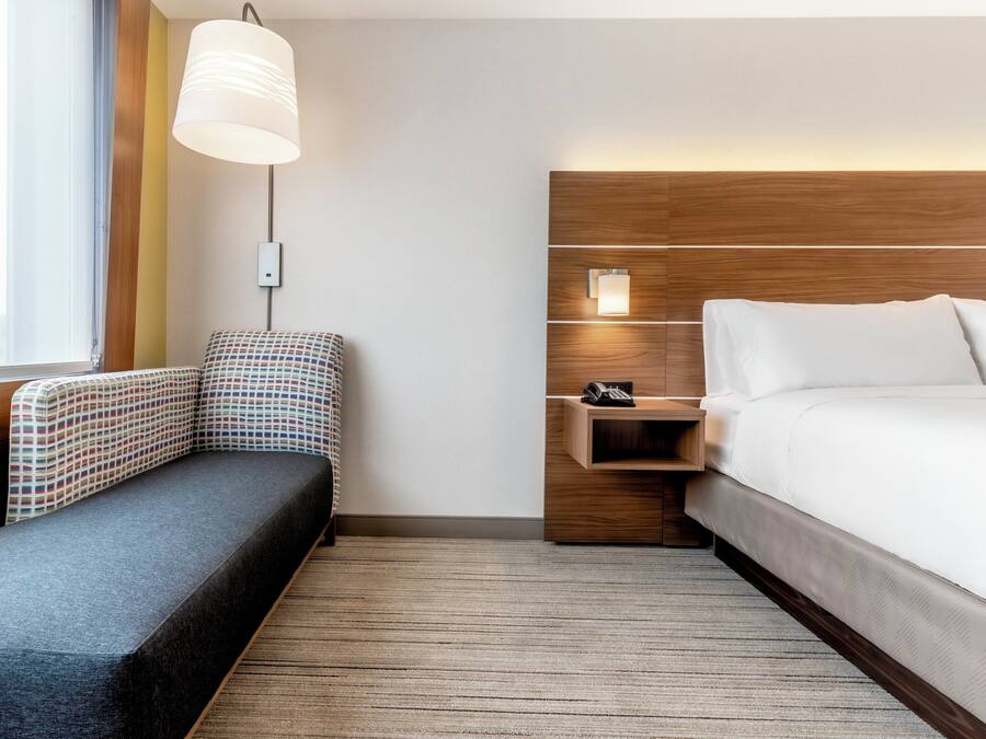 Habitació d'hotel amb un llit, una taula de treball amb un telèfon, una cadira, una làmpada i una finestra amb cortines.