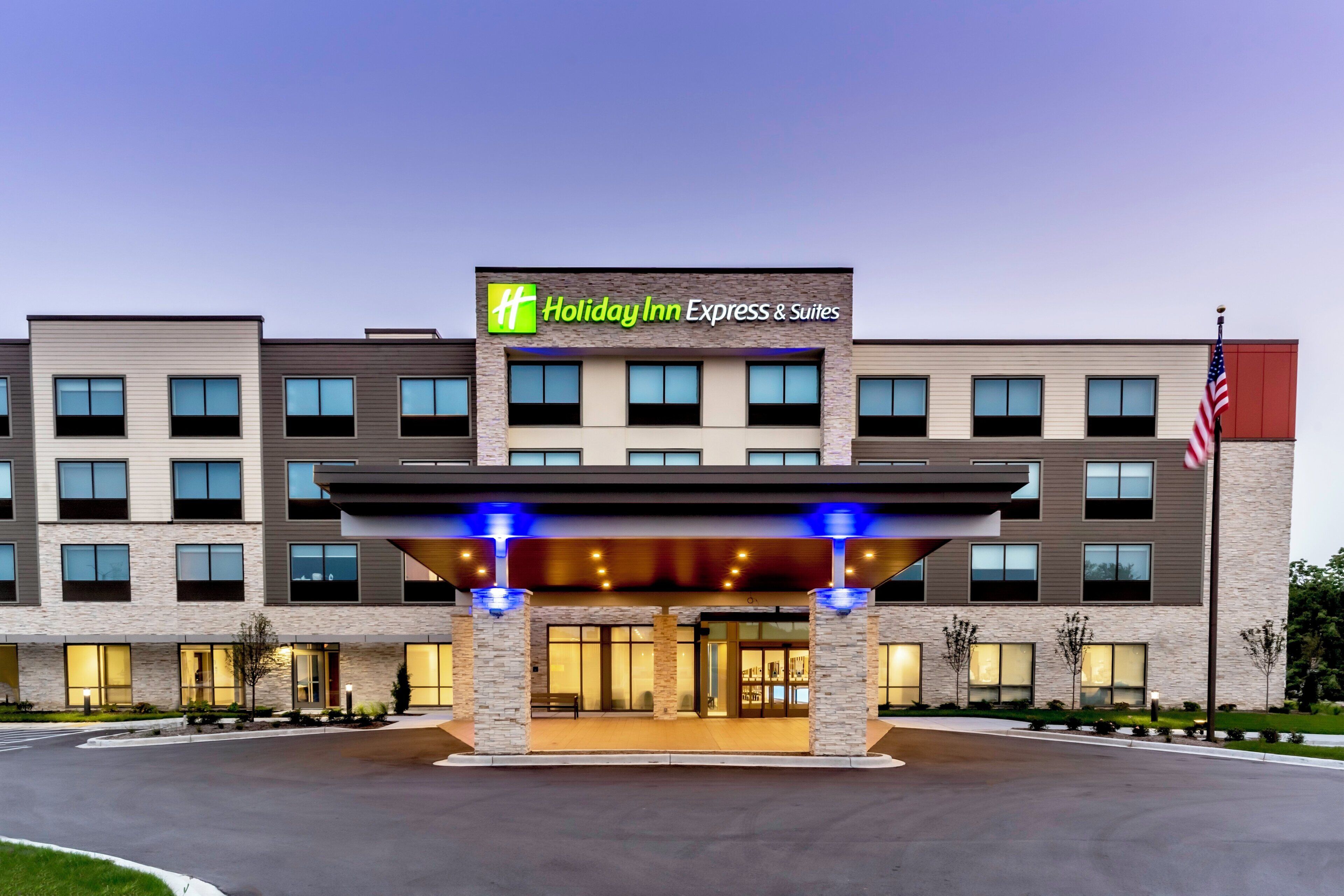 Un bâtiment de la chaîne Holiday Inn Express & Suites, doté d’une façade moderne, de nombreuses fenêtres et arborant le drapeau américain.