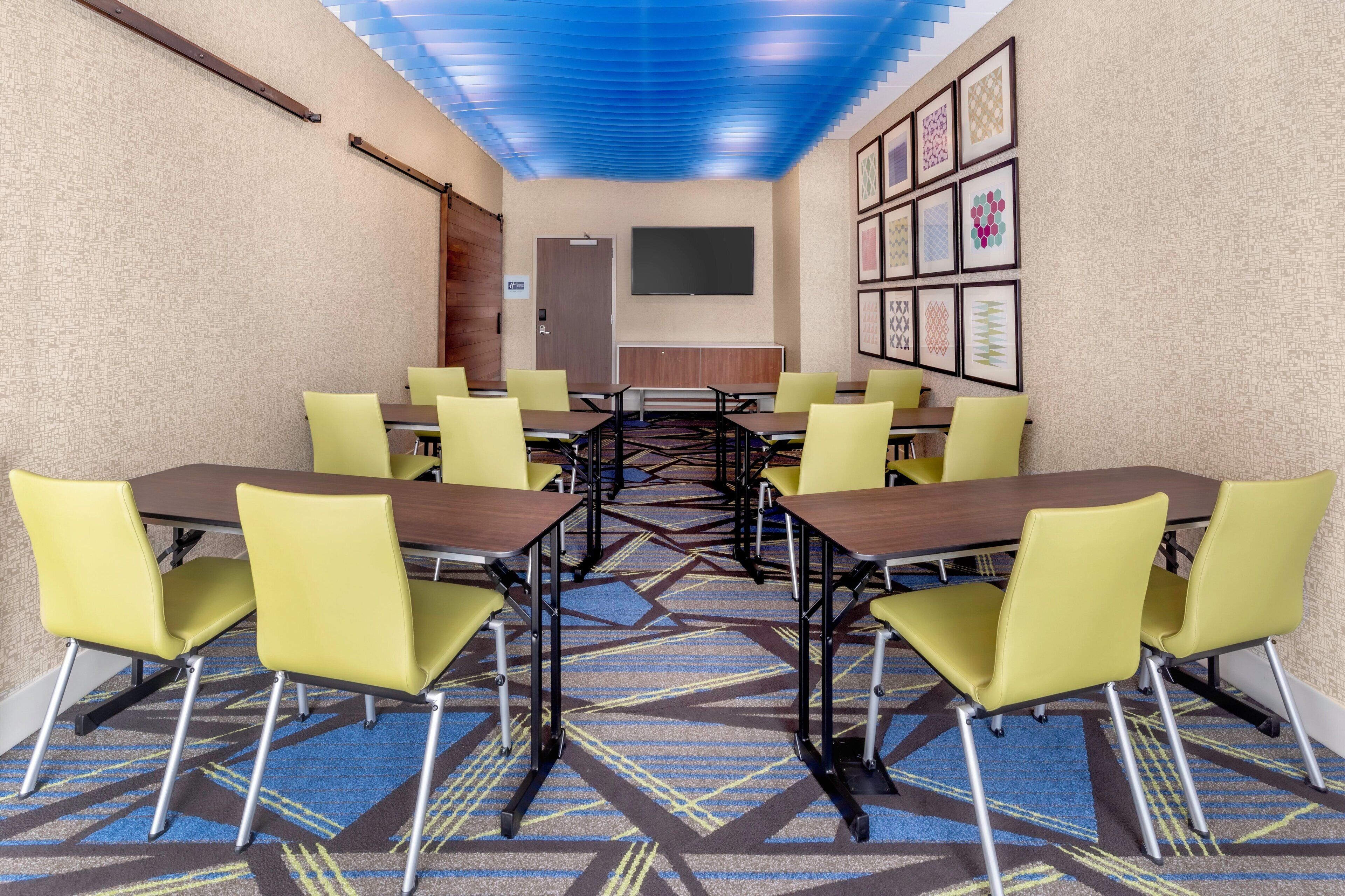 A conference room with tables and chairs, a patterned carpet, and framed artwork on the walls.