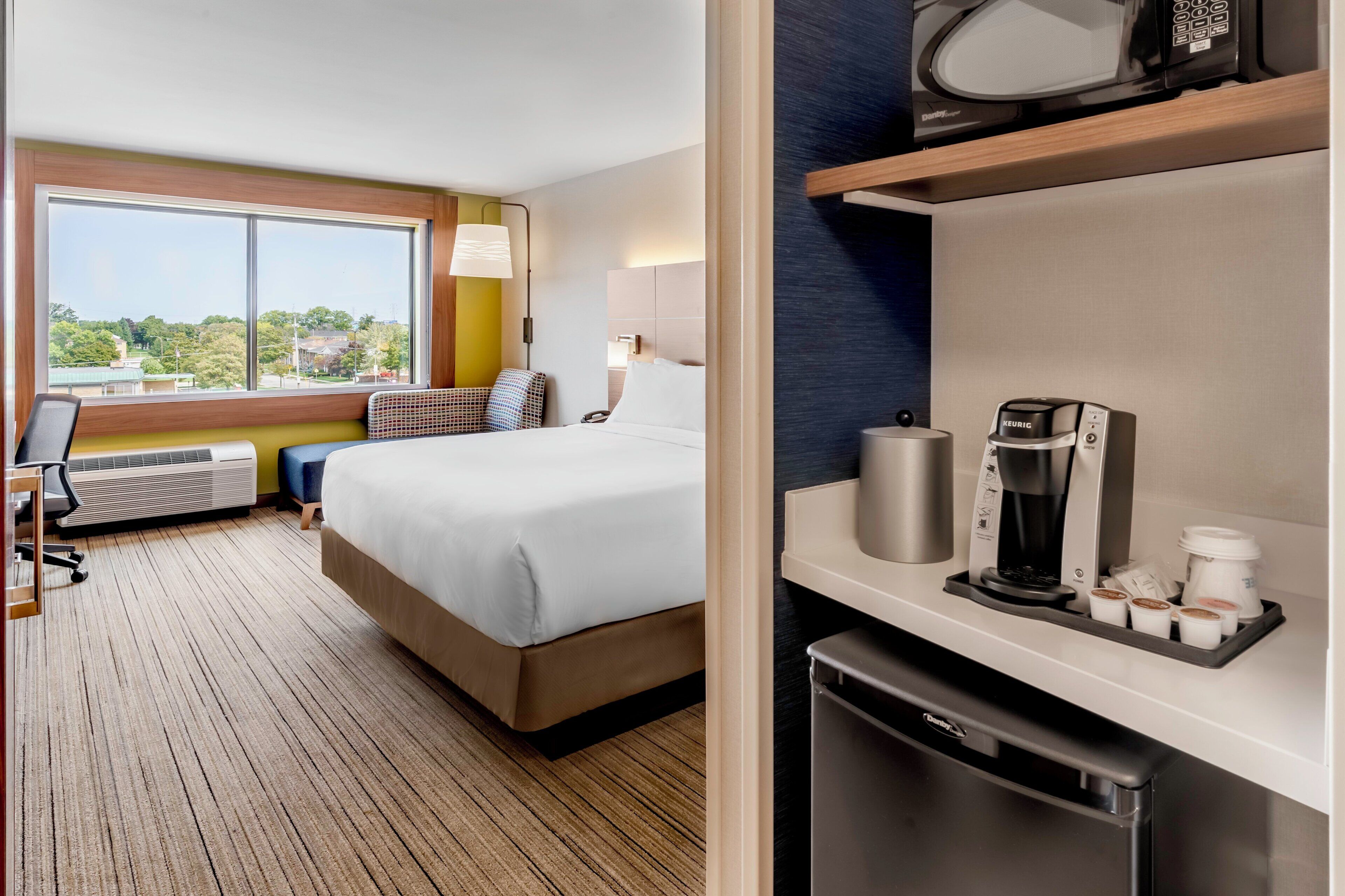 Habitación de hotel con cama, escritorio, microondas, cafetera y vistas al exterior.