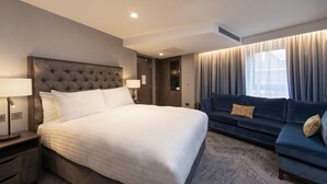 A hotel room with a large bed, a sofa, a nightstand, and a window with curtains. - voco Edinburgh-Haymarket by IHG (Edinburgh)