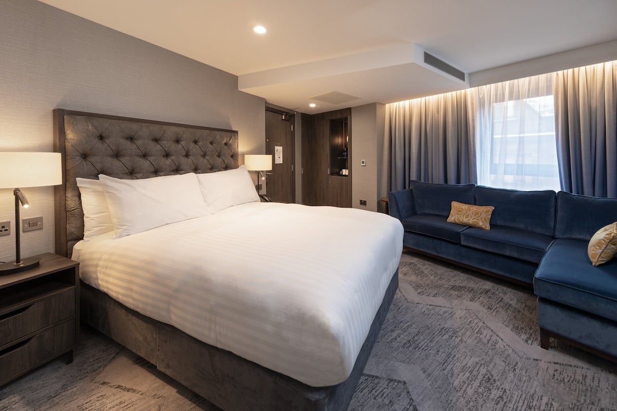 A hotel room with a large bed, a sofa, a nightstand, and a window with curtains.
