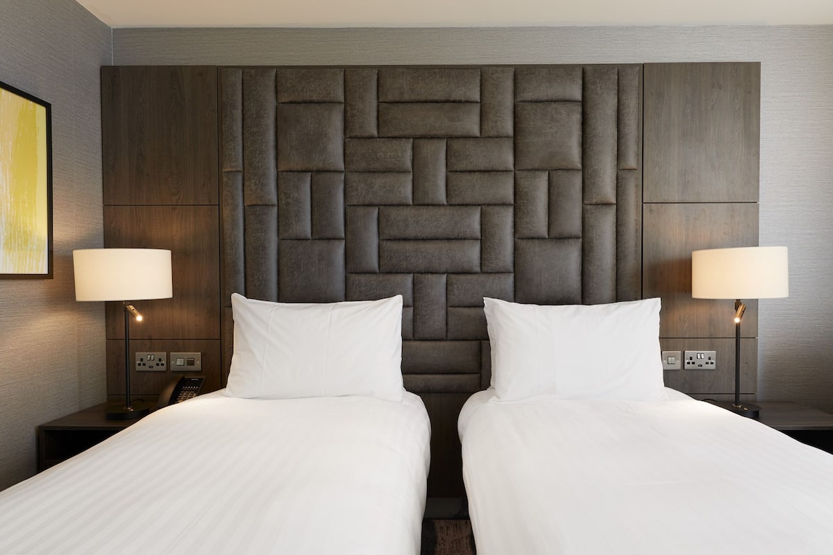 A hotel room with two beds, a modern headboard, bedside lamps, and a small table with a phone.