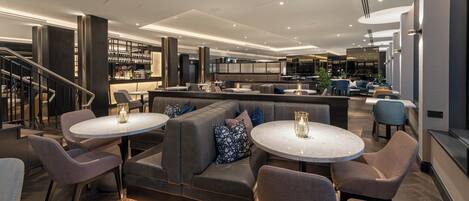 A modern lounge area with sofas, round tables, and a bar.
