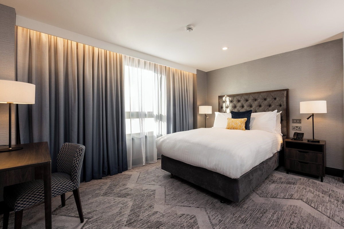 Une chambre d’hôtel avec un grand lit, un bureau, une chaise et une table de chevet avec une lampe.