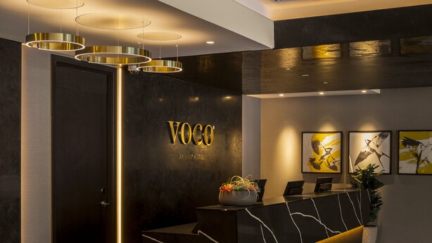 A reception desk with a modern design, a logo above it, and three framed artworks on the wall. - voco Edinburgh-Haymarket by IHG (Edinburgh)