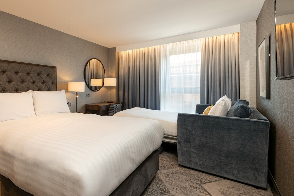 A hotel room with a large bed, bedside tables, a desk, and a chair.