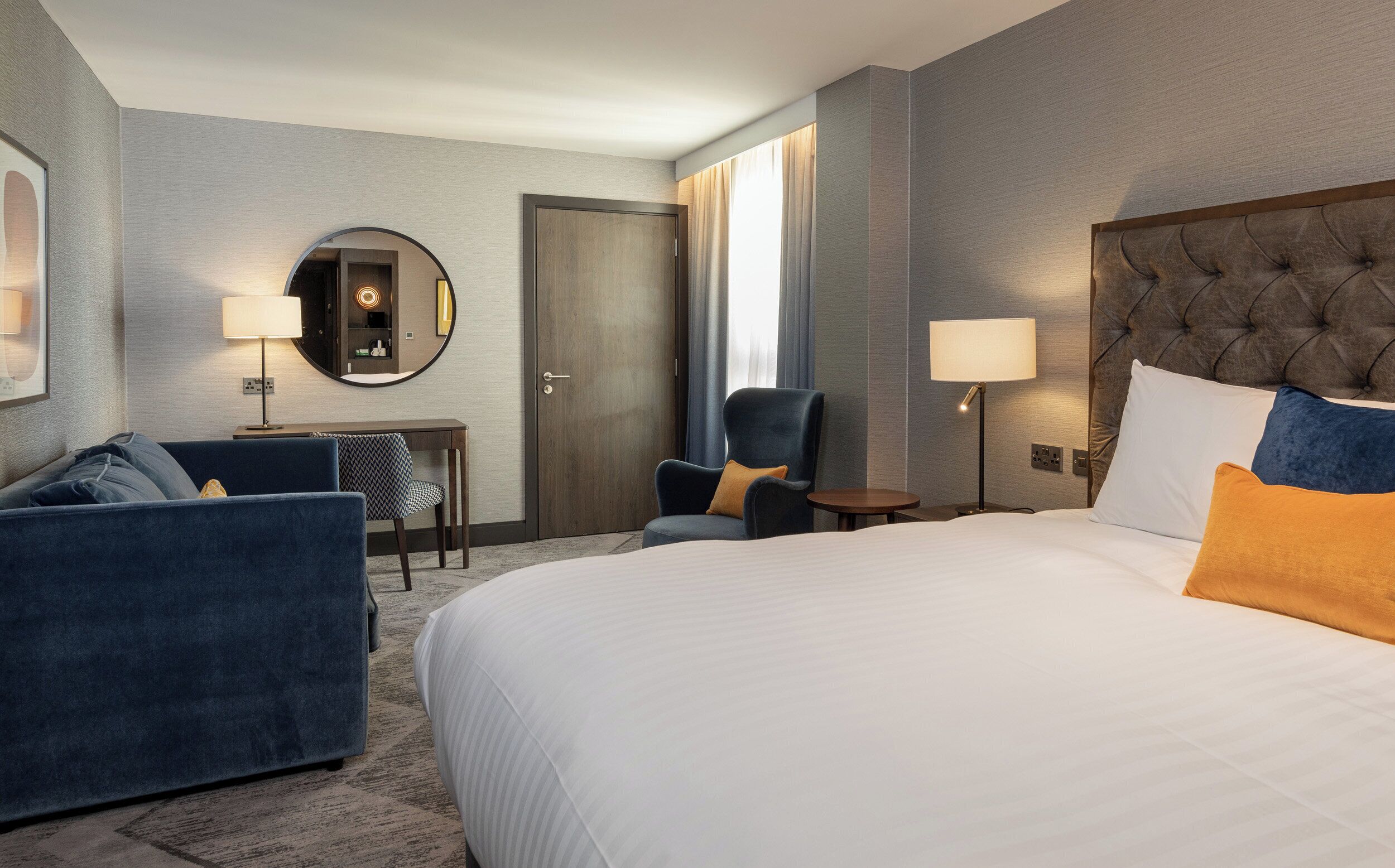 Une chambre d’hôtel avec un grand lit, un coin salon comprenant un canapé et des fauteuils, une petite table et un miroir.