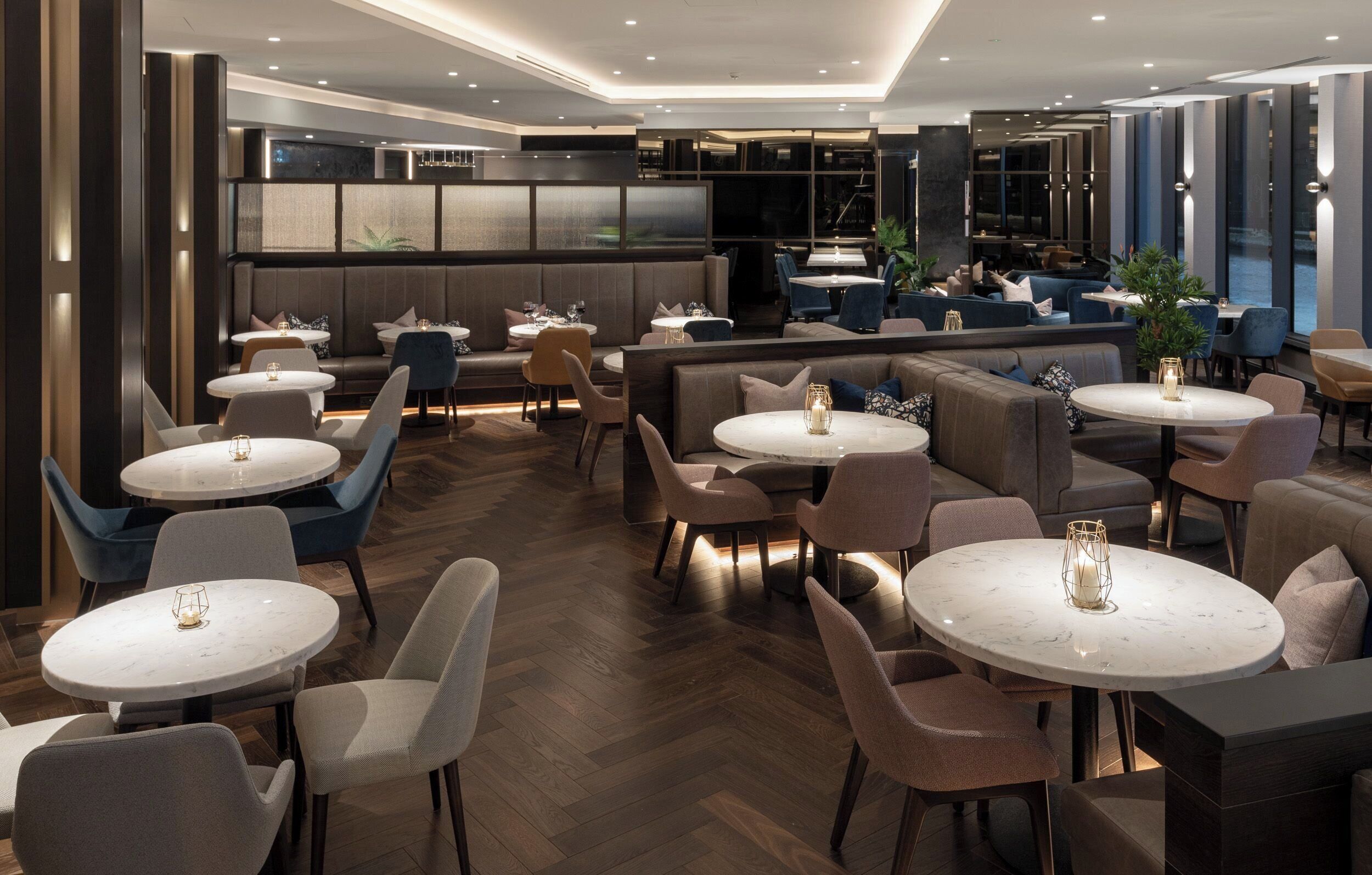 A modern restaurant with round tables, cushioned seating, and a bar area.