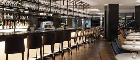 A bar area with multiple seating options, including bar stools and tables, and a variety of bottles and glasses on shelves.