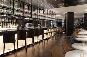 Un espace bar offrant différentes options de sièges, notamment des tabourets et des tables, ainsi qu’une variété de bouteilles et de verres exposés sur des étagères.