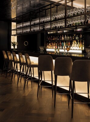 A bar area with multiple stools, a glass display case with bottles, and a bar counter. - voco Edinburgh-Haymarket by IHG (Edinburgh)