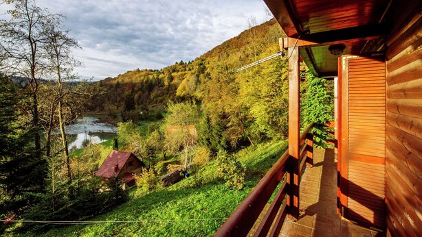 A wooden cabin with a balcony overlooking a river and forested hills. - Serene Holiday Home in Dolus With Private Garden (Brod Moravice)