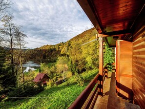 A wooden cabin with a balcony overlooking a river and forested hills. - Serene Holiday Home in Dolus With Private Garden (Brod Moravice)