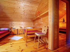 A wooden cabin room with a bed, a chair, a nightstand, and a shelf with flowers. - Serene Holiday Home in Dolus With Private Garden (Brod Moravice)