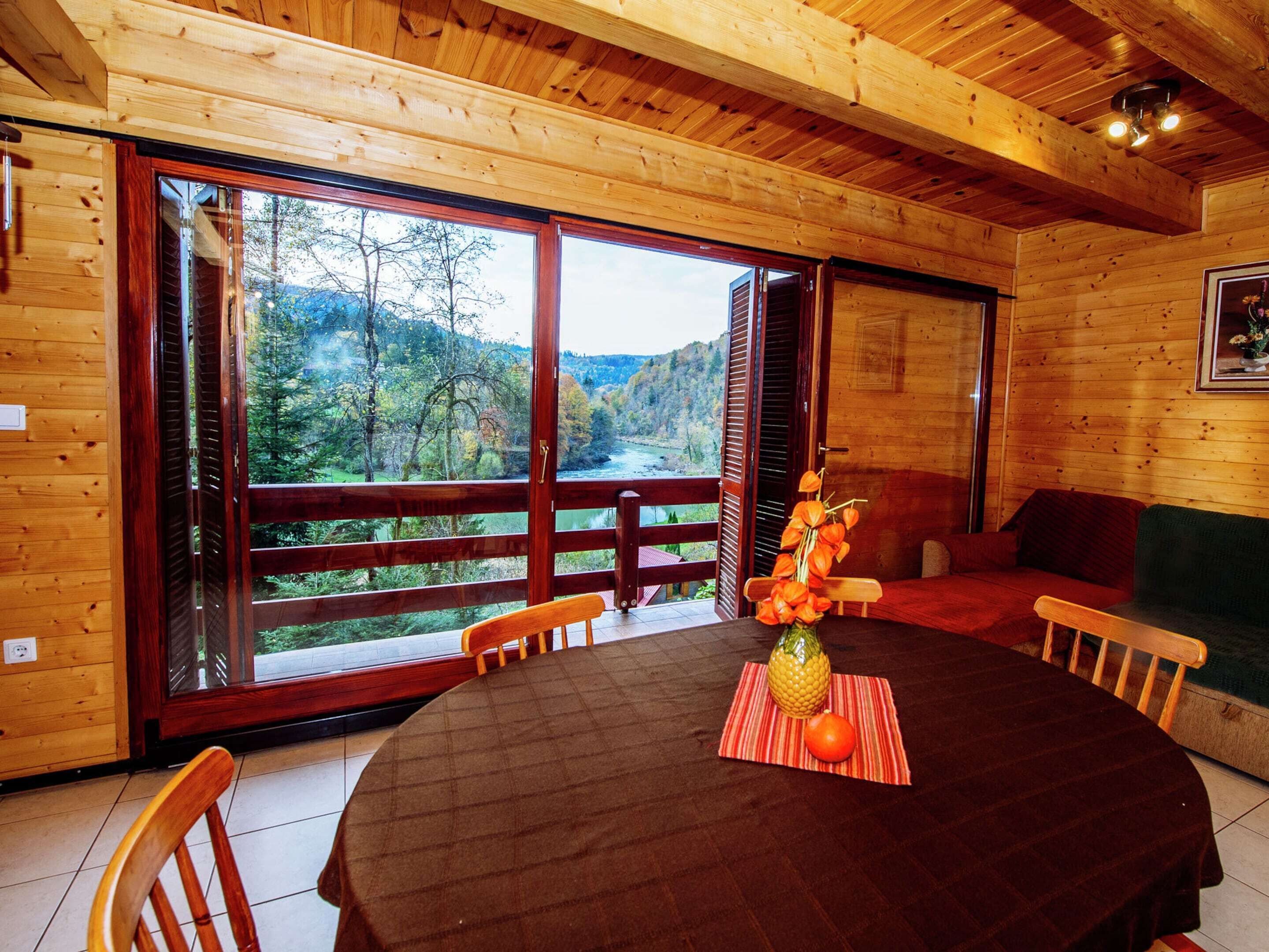 Una cabaña de madera con una amplia mesa de comedor, sillas y vistas a un área boscosa a través de grandes ventanales.