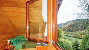 A cozy wooden cabin room with a large window, a bed with green bedding, a small table, and a view of a green valley. - Serene Holiday Home in Dolus With Private Garden (Brod Moravice)