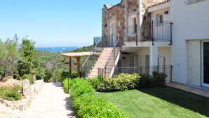 A multi-story building with a stone facade, a staircase leading to a balcony, and a view of the sea.