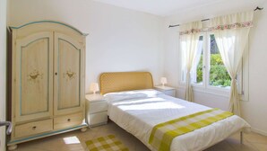 A bedroom with a bed, nightstands, a wardrobe, a window with curtains, and a checkered rug.