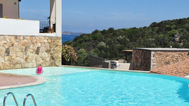 A swimming pool with a stone wall and a view of the sea.