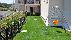 A residential building with a balcony, a swing set, and a well-maintained lawn.