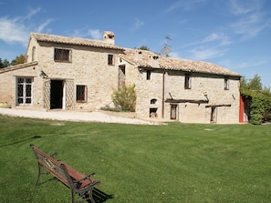 A stone building with a tiled roof, a small garden, and a bench. - Belvilla by OYO Appartamento del Caminetto (Treia)