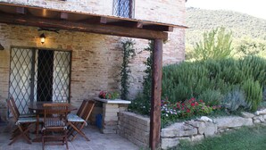 A patio area with a wooden table and chairs, a brick wall, and a garden with various plants and flowers. - Belvilla by OYO Appartamento del Caminetto (Treia)