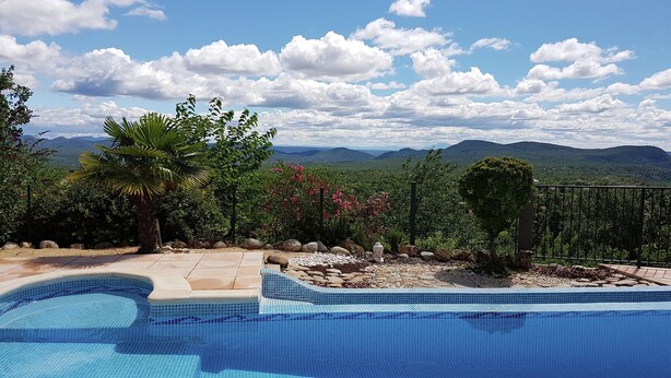 A swimming pool with a view of mountains, surrounded by landscaped garden and a metal fence. - Courry Views: Pool & Nature (Courry)