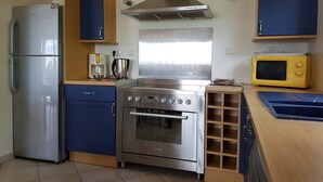 A compact kitchen with a stainless steel refrigerator, a stove, a microwave, and wooden cabinets. - Courry Views: Pool & Nature (Courry)
