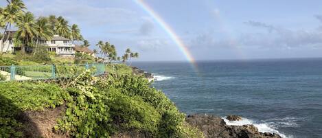 Une vue sur la côte, avec un arc-en-ciel, une végétation luxuriante et une maison offrant une vue sur l’océan.