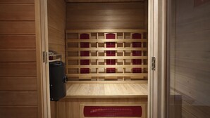 Una sauna de fusta amb un banc, un escalfador i una prestatgeria amb contenidors vermells.