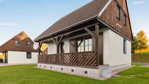 Une maison moderne à deux étages, dotée d’un toit en pente, de grandes fenêtres et d’une terrasse en bois.