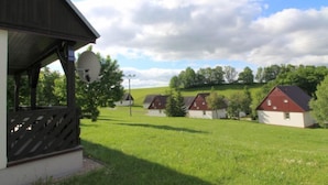 Un paysage rural avec un bâtiment en bois surmonté d’une antenne parabolique, entouré de champs verdoyants et de plusieurs petites maisons aux toits rouges.