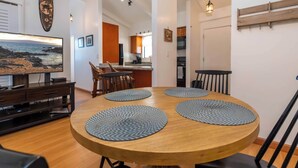 Un coin repas avec une table ronde en bois, quatre chaises noires et trois sets de table en fibres tressées. Un téléviseur est fixé au mur, au-dessus de la table.
