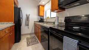 Une cuisine moderne dotée de plans de travail en granit, d’un réfrigérateur noir, d’armoires en bois, d’un lave-vaisselle, d’une cuisinière et d’une fenêtre avec un rideau.