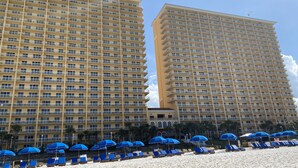 A hotel with multiple floors, balconies, and a beach area with sun loungers and umbrellas.