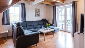 Un salon moderne avec un canapé gris, une petite table sur laquelle se trouvent une bouteille et des fleurs, et un tableau accroché au mur.