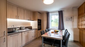 Une cuisine moderne avec des meubles en bois, une table à manger avec des chaises, une fenêtre avec des rideaux et un luminaire au plafond.