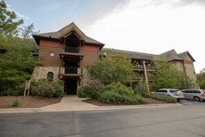 A two-story building with a stone facade, a balcony on the upper floor, and a parking lot in front.
