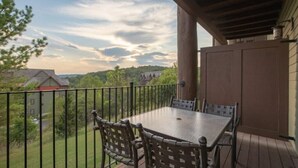 A covered outdoor patio with a table and chairs, surrounded by a wooden deck and a metal railing. - Big Cedar | Rustic Retreat | Pools, Lake & Adventure (Ridgedale)