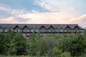 A multi-story hotel with a row of rooms featuring a consistent architectural style, surrounded by dense forest. - Big Cedar | Rustic Retreat | Pools, Lake & Adventure (Ridgedale)