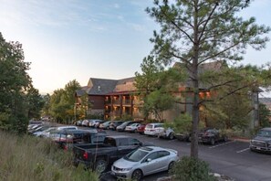 A parking lot with several cars, a building with a sloped roof, and a tree in the foreground.