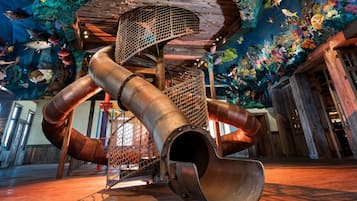 A large, industrial-style structure with multiple pipes and a mesh enclosure, set against a backdrop of colorful marine life decorations.