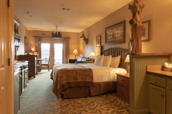 A hotel room with a large bed, a wooden headboard, a desk with a chair, a dresser, and a large tree trunk decoration.