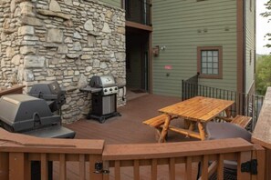A wooden deck with a stone wall, a grill, and a table with chairs. - Big Cedar | Rustic Retreat | Pools, Lake & Adventure (Ridgedale)
