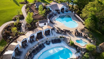 A resort with multiple swimming pools, covered outdoor seating areas, and a well-maintained lawn.